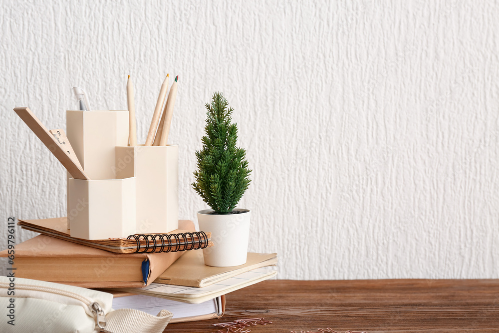 Holder with different stationery, houseplant and notebooks on wooden desk