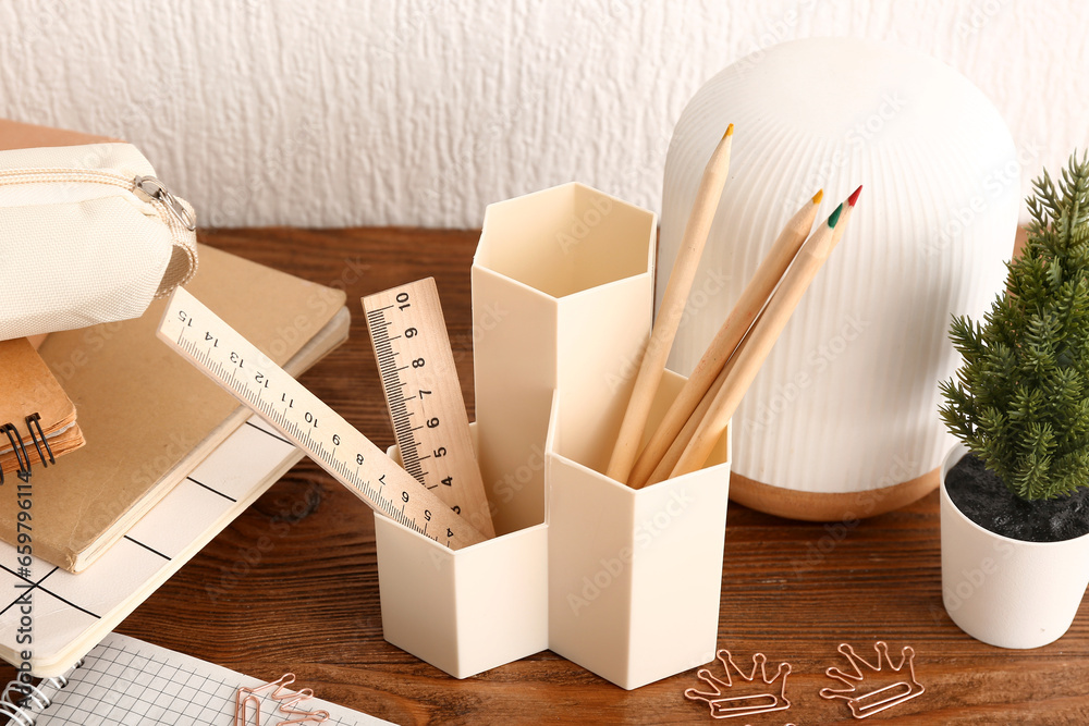 Holder with different stationery, houseplant and notebooks on wooden desk, closeup