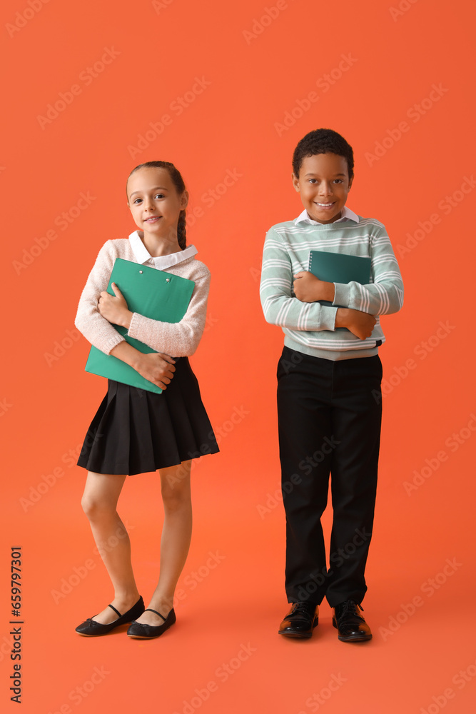 Little classmates in stylish uniform with notebooks on orange background