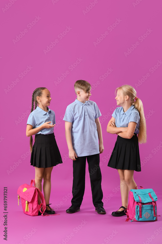 Little classmates in stylish uniform with backpacks on purple background