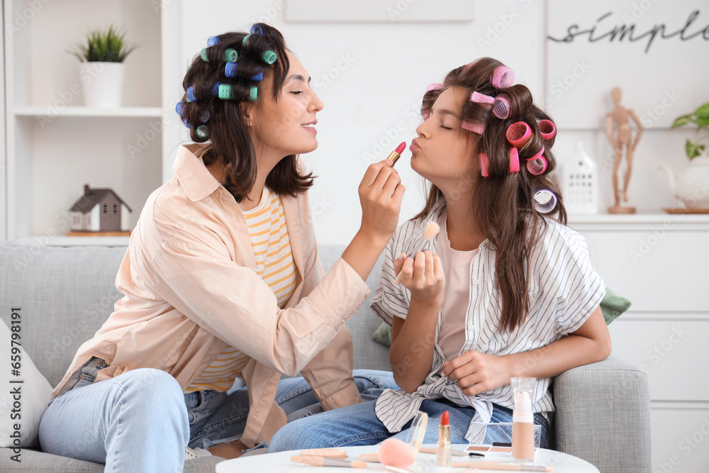 Little girl and her mother with hair curlers doing makeup at home