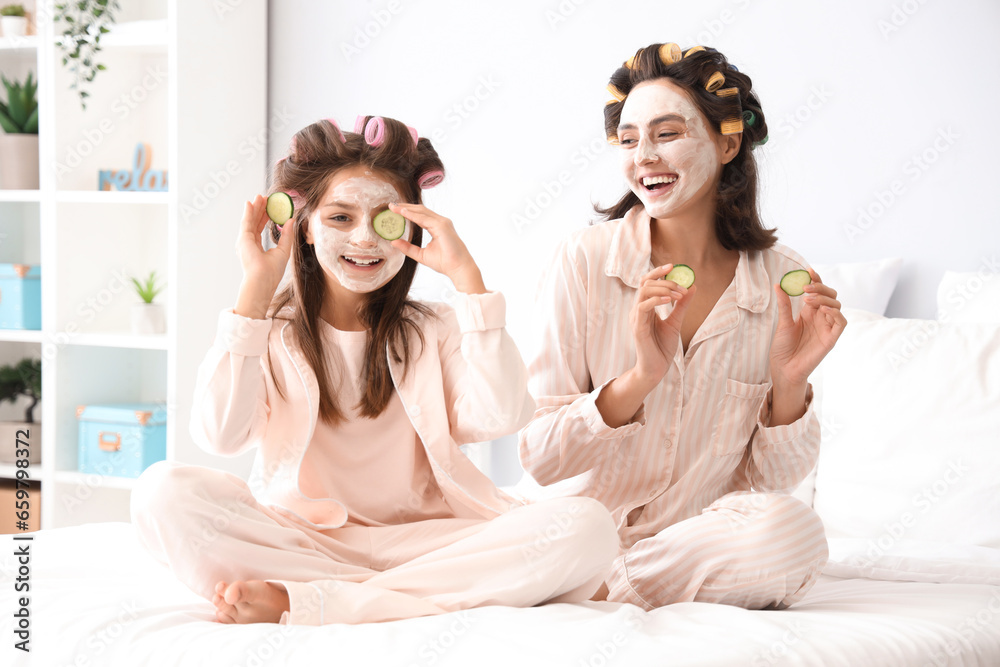 Little girl and her mother with hair curlers applying facial mask in bedroom