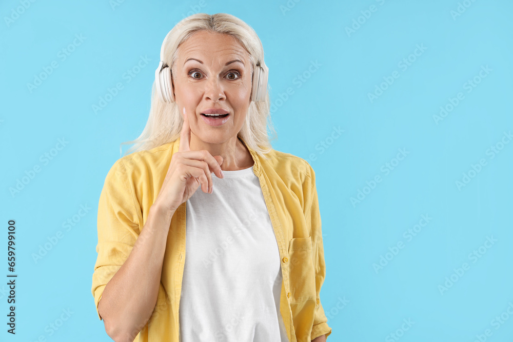 Thoughtful mature woman in headphones on blue background