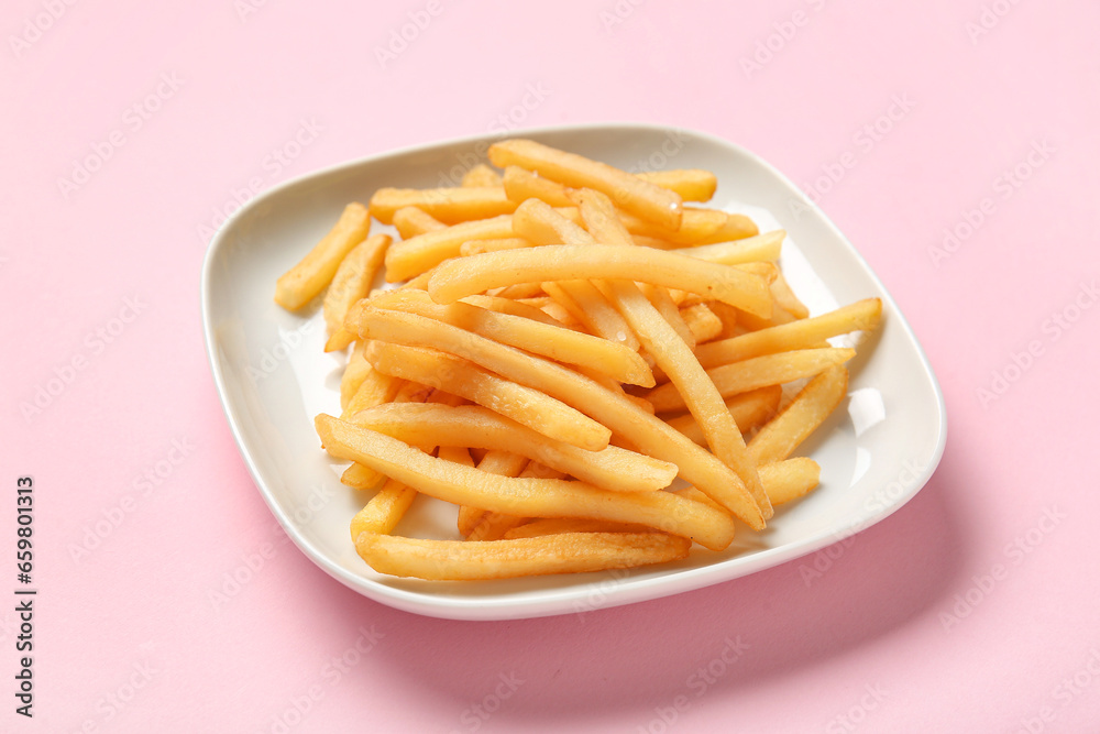 Plate with tasty french fries on pink background