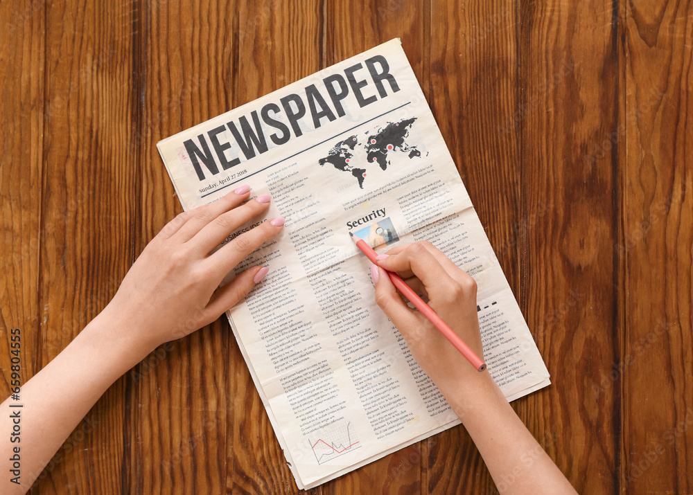 Woman marking text in newspaper with pencil on wooden background