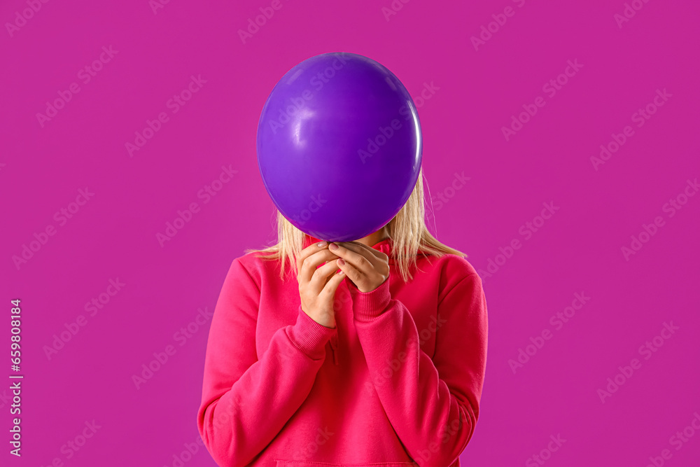 Beautiful young woman in stylish hoodie with balloon on purple background