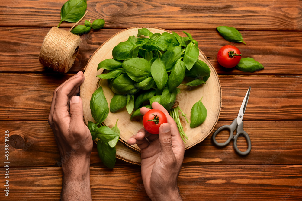 Male hands with board of fresh green basil and tomatoes on wooden background