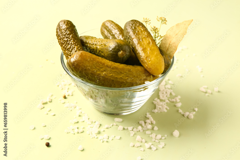 Glass bowl with tasty pickled cucumbers and different spices on green background