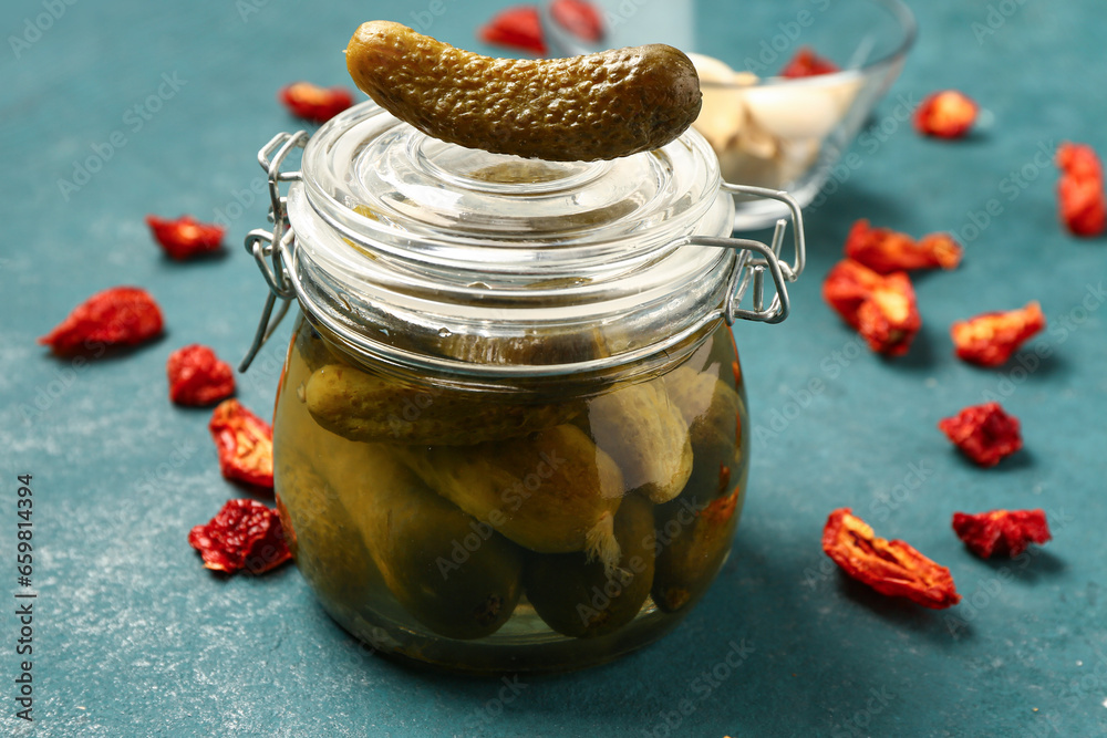 Jar with tasty pickled cucumbers and dried tomatoes on color background