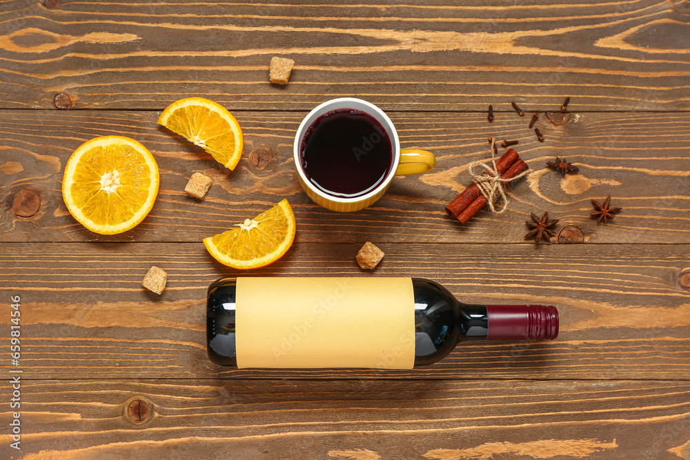 Cup and bottle of red wine with different spices on wooden background