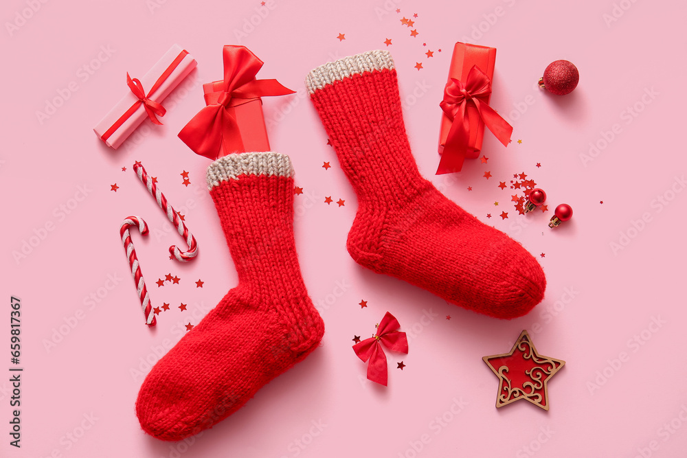 Beautiful Christmas socks with gift boxes and decorations on pink background