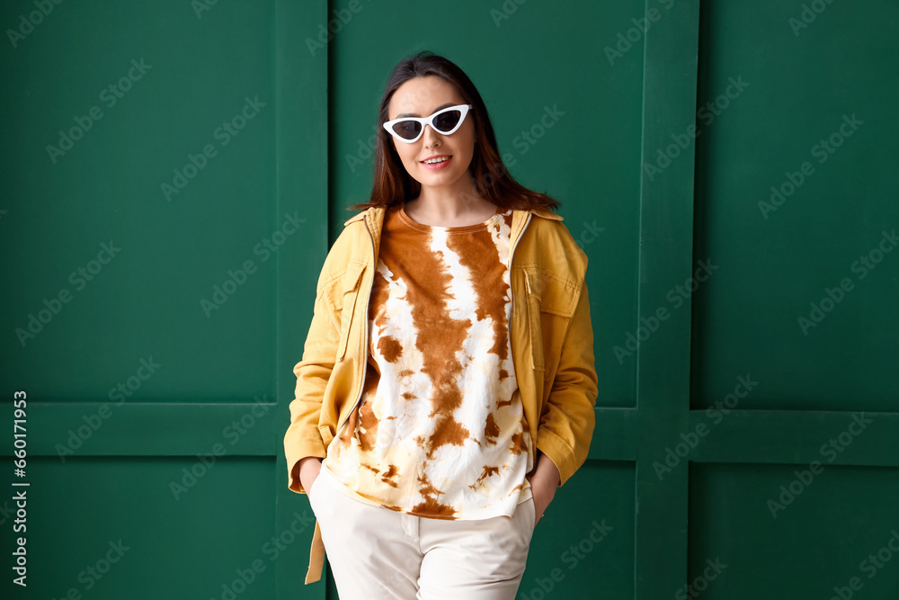 Stylish young woman in tie-dye t-shirt on green background