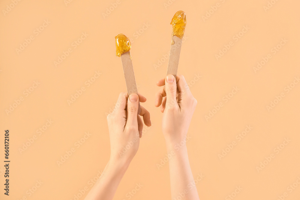 Female hands holding spatulas with sugaring paste on beige background