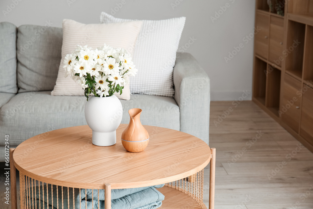 Vase with blooming chrysanthemum flowers on wooden coffee table in interior of living room