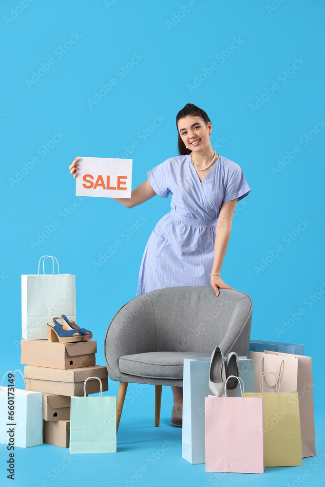 Female seller with sale sign, shoe boxes, shopping bags and armchair on blue background