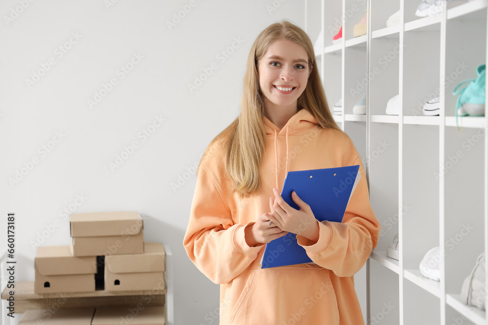 Female seller with clipboard revising in shoe shop