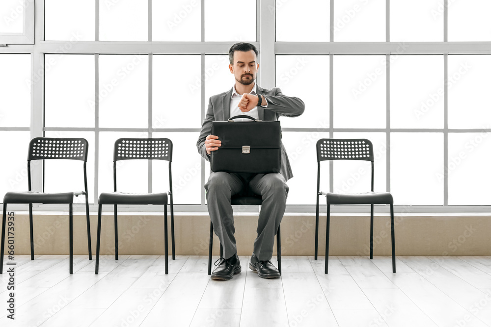 Young man looking at wristwatch while waiting for job interview in office