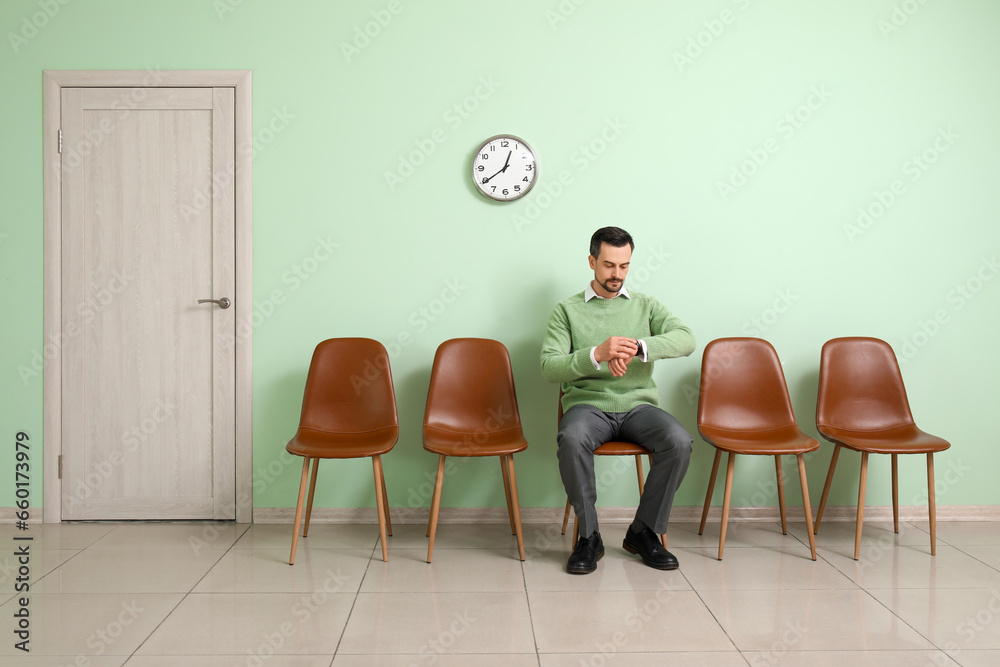 Young man looking at wristwatch while waiting for job interview in room