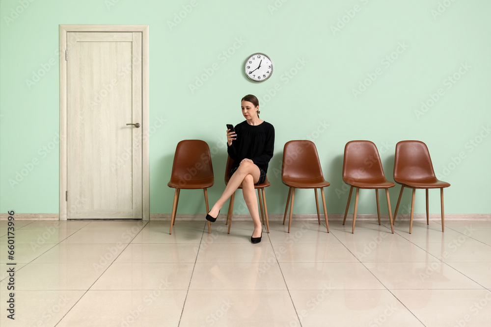 Young woman with mobile phone waiting for job interview in room