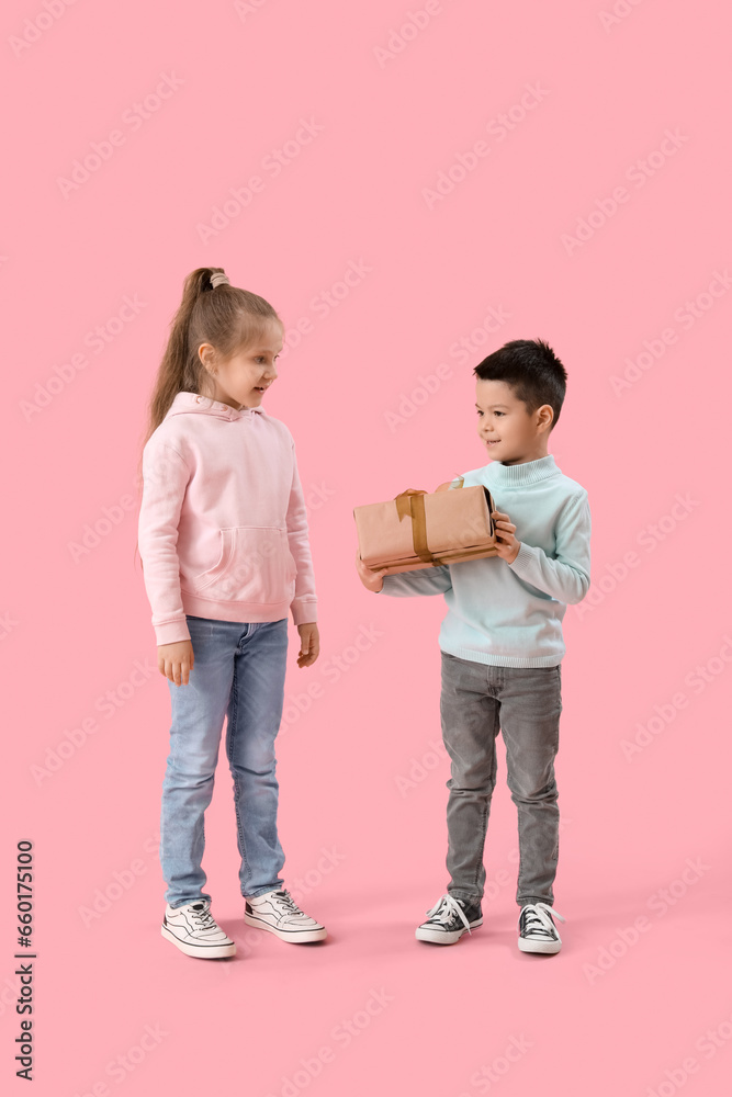 Cute little children in sweaters with gift on pink background