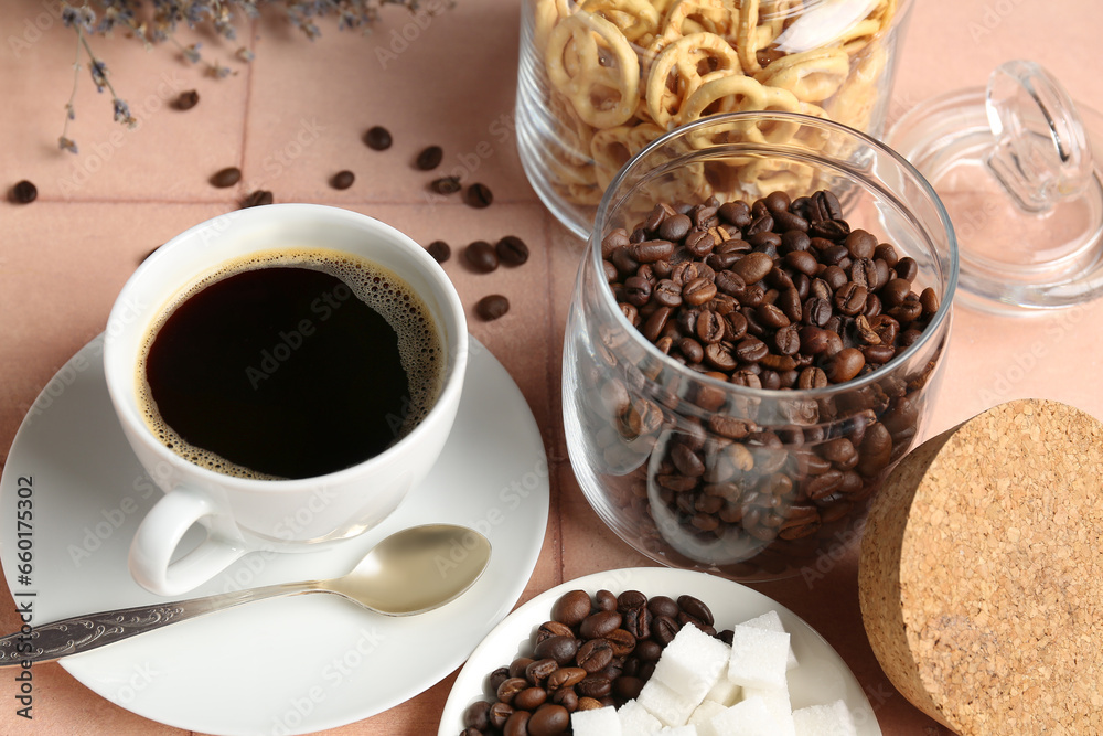 Cup of coffee and jar with beans on beige tile background