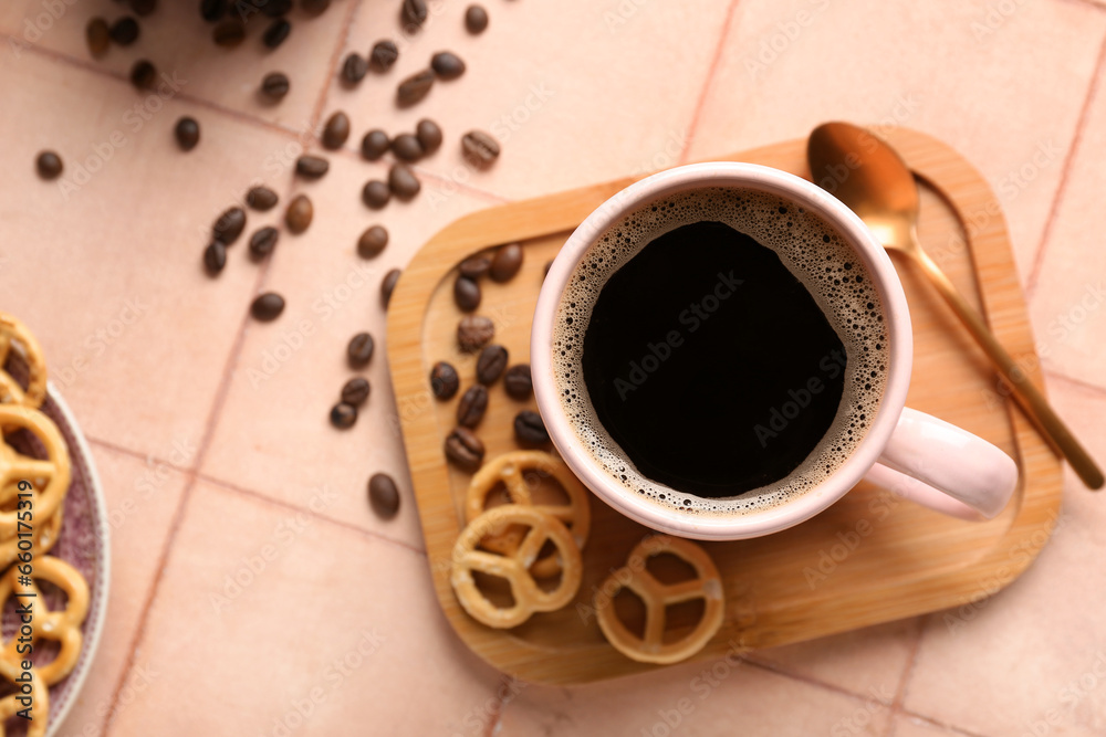 Cup of coffee with beans and pretzels on beige tile background