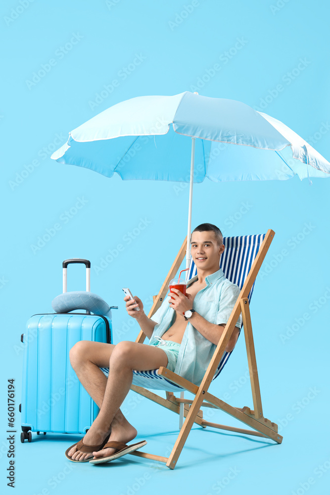 Teenage boy with soda using mobile phone in deck chair on blue background