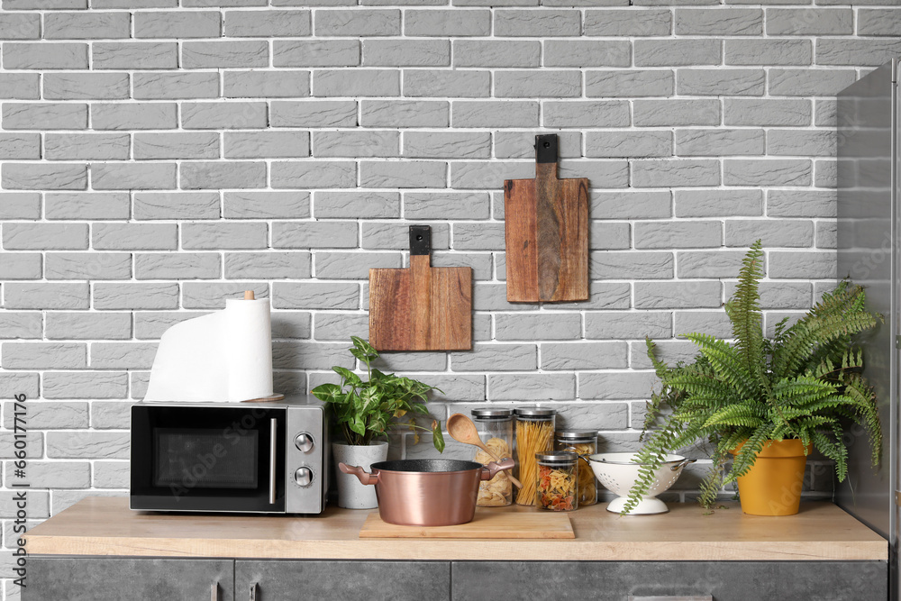 Wooden countertop with microwave oven, houseplants and utensils in modern kitchen