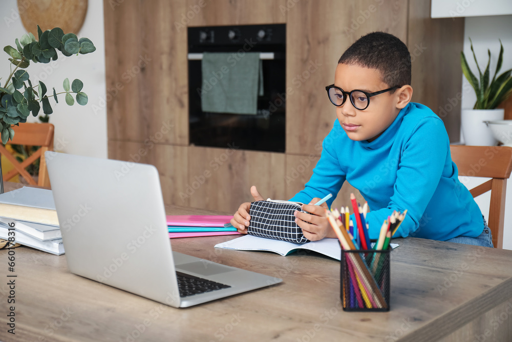 Little African-American boy studying online with laptop in kitchen