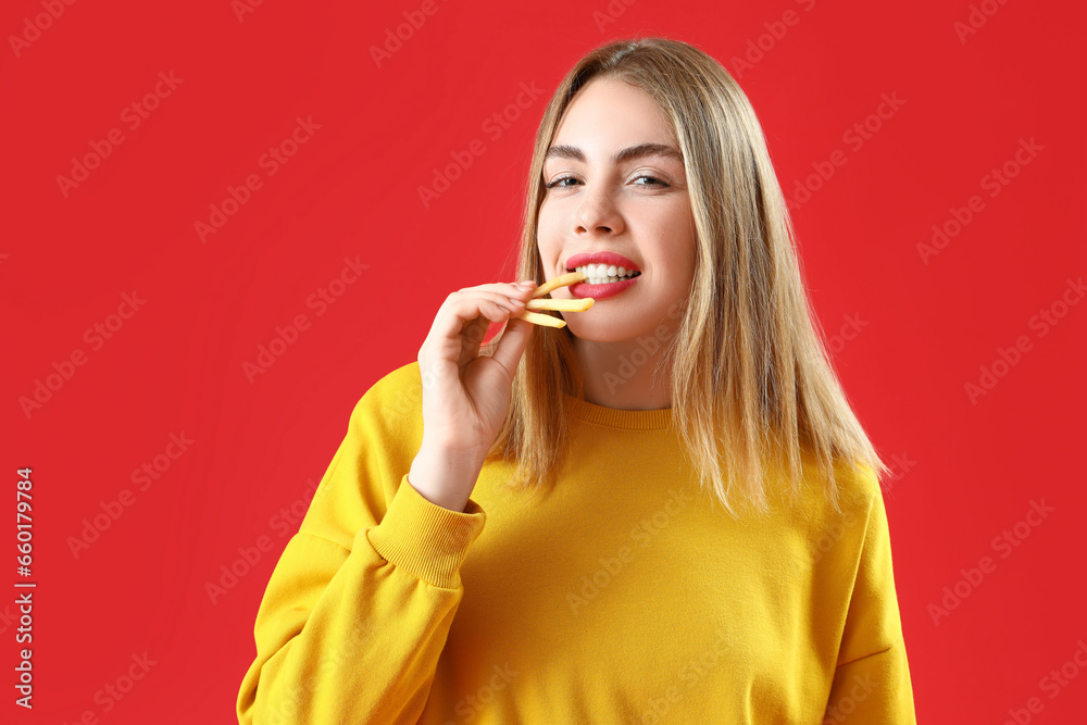 Beautiful young woman eating french fries on red background