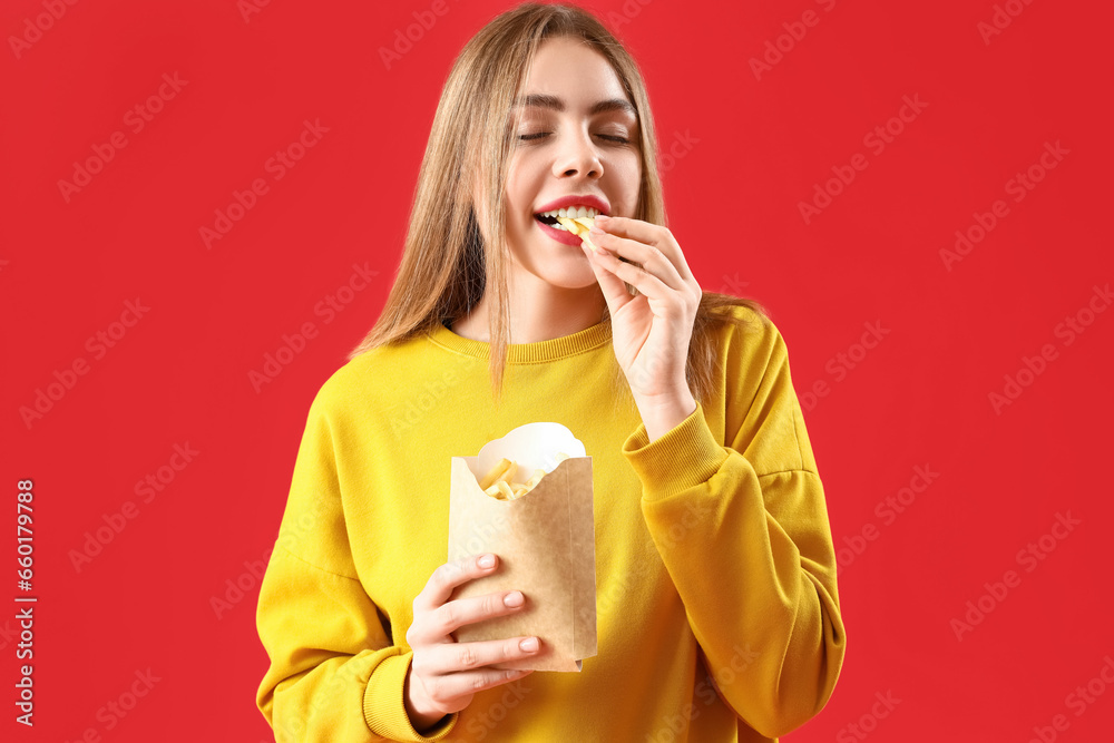 Beautiful happy young woman eating french fries on red background