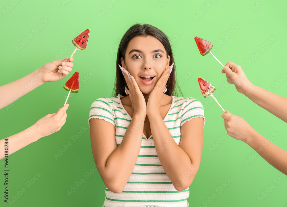 Beautiful surprised young woman and hands with watermelon lollipops on green background