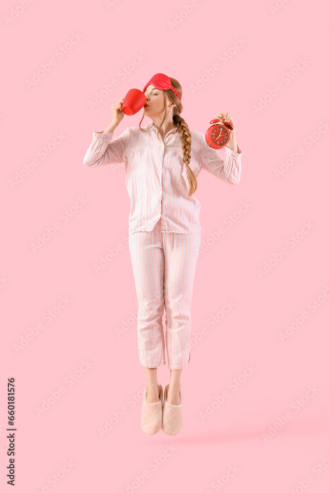 Beautiful young woman with cup of coffee and alarm clock jumping on pink background