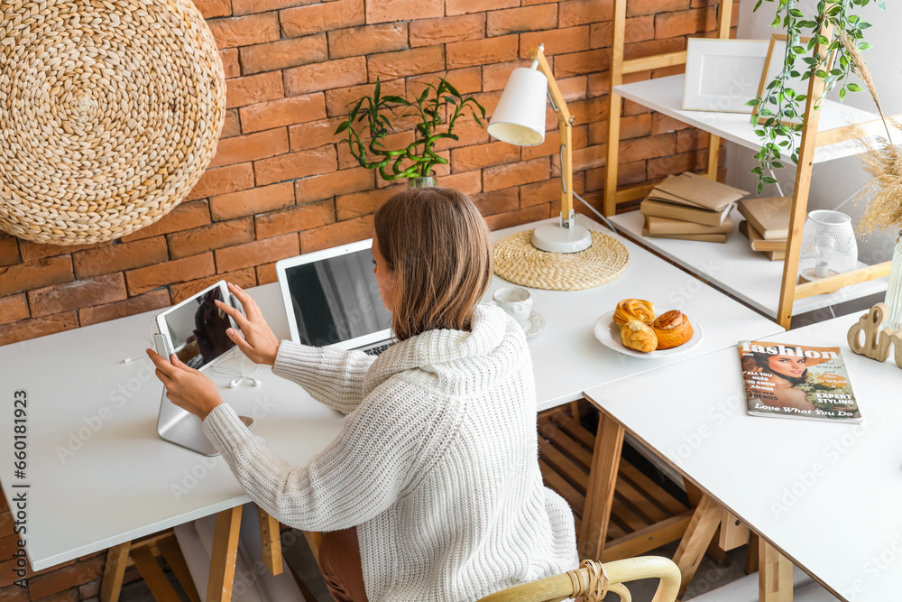 Young woman working with tablet computer at table in office, back view