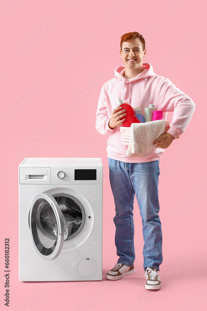 Young man with detergents near washing machine on pink background