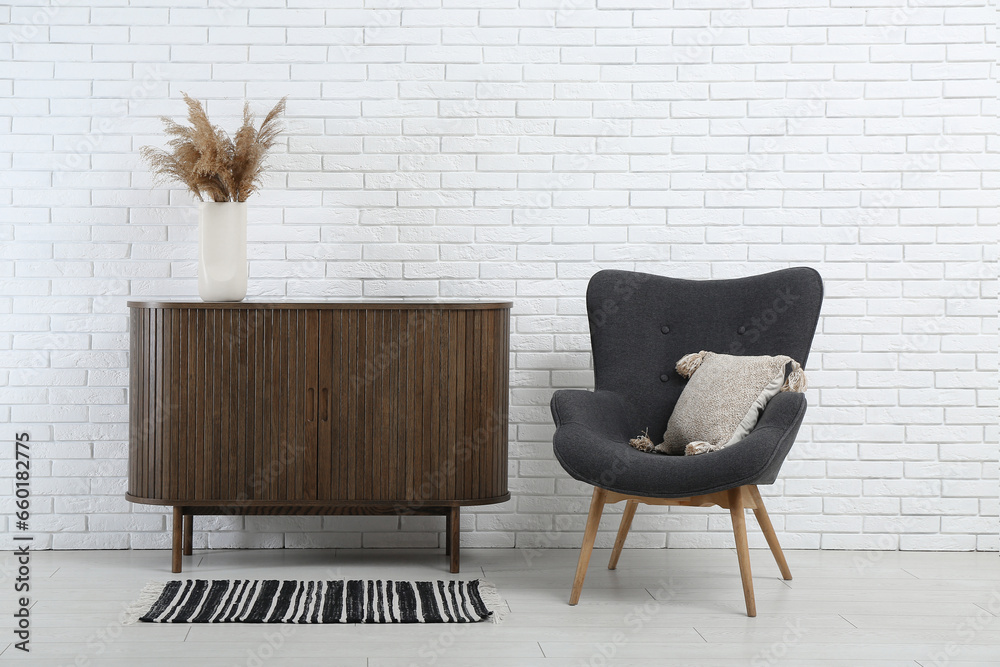 Stylish armchair and wooden cabinet near light brick wall