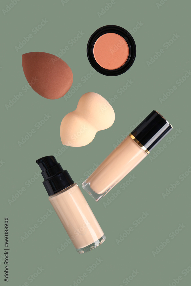 Bottles of liquid foundation, concealer and makeup sponges flying on green background