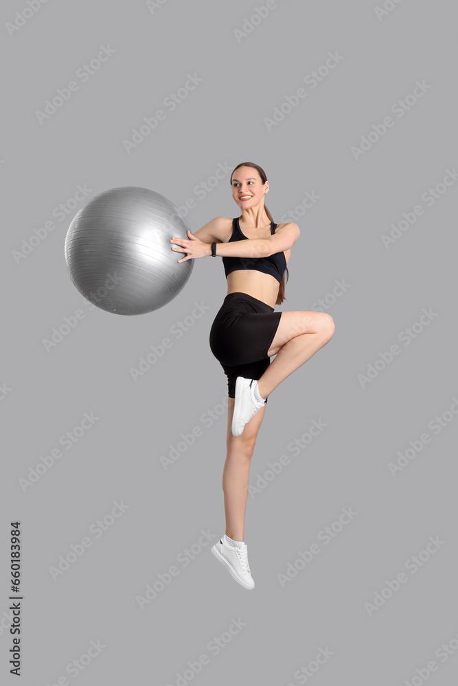 Sporty young woman training with fitball on light background