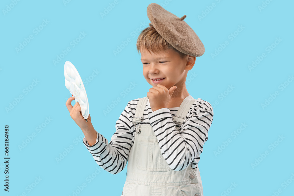 Thoughtful little artist with paint palette on blue background