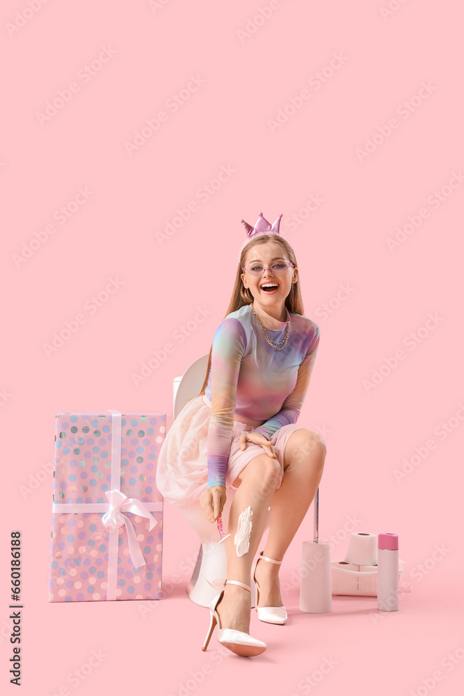 Young woman sitting on toilet bowl and birthday gift against pink background