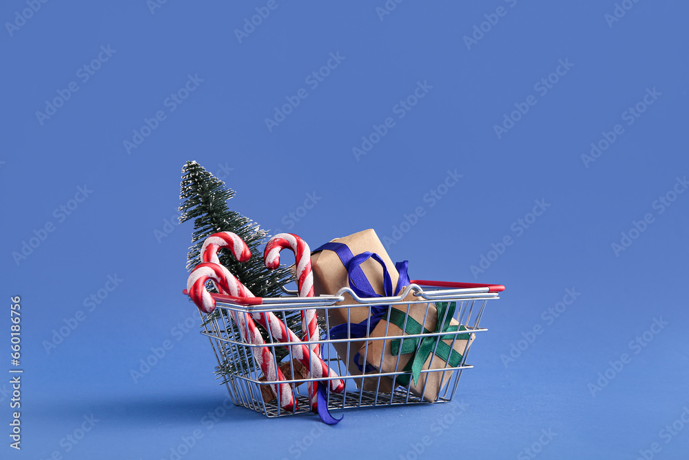 Shopping basket with Christmas tree, candy cane toys and gift boxes on blue background