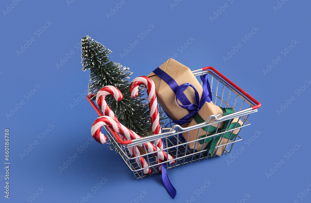 Shopping basket with Christmas tree, candy cane toys and gift boxes on blue background