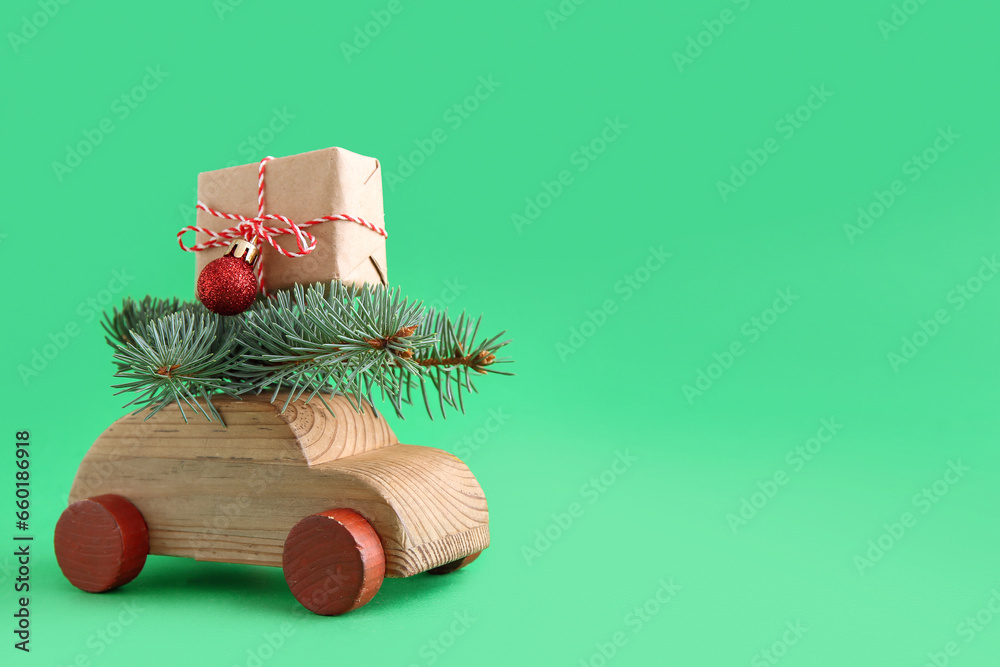 Wooden toy car with Christmas tree branches and gift box on green background