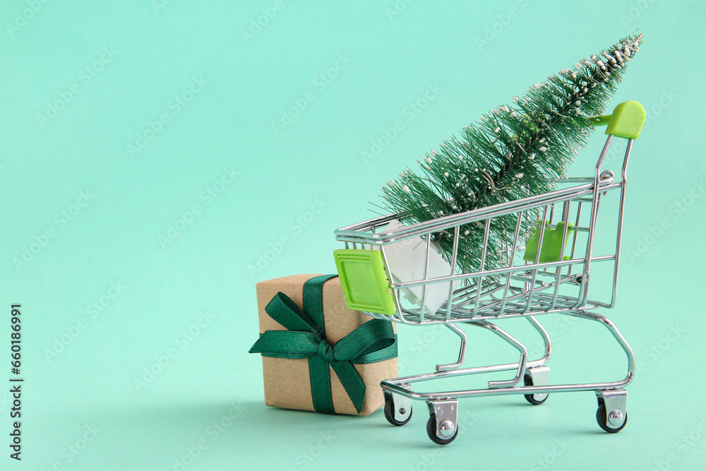 Shopping cart with Christmas tree and gift box on green background