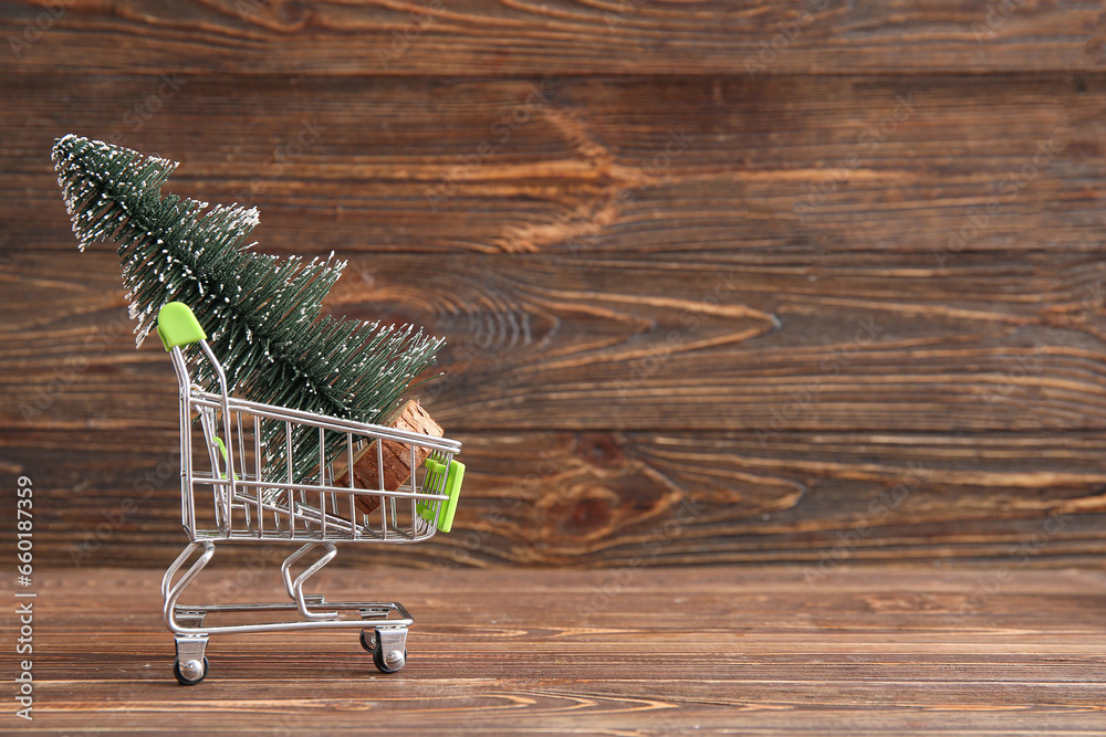 Shopping cart with Christmas tree on wooden background