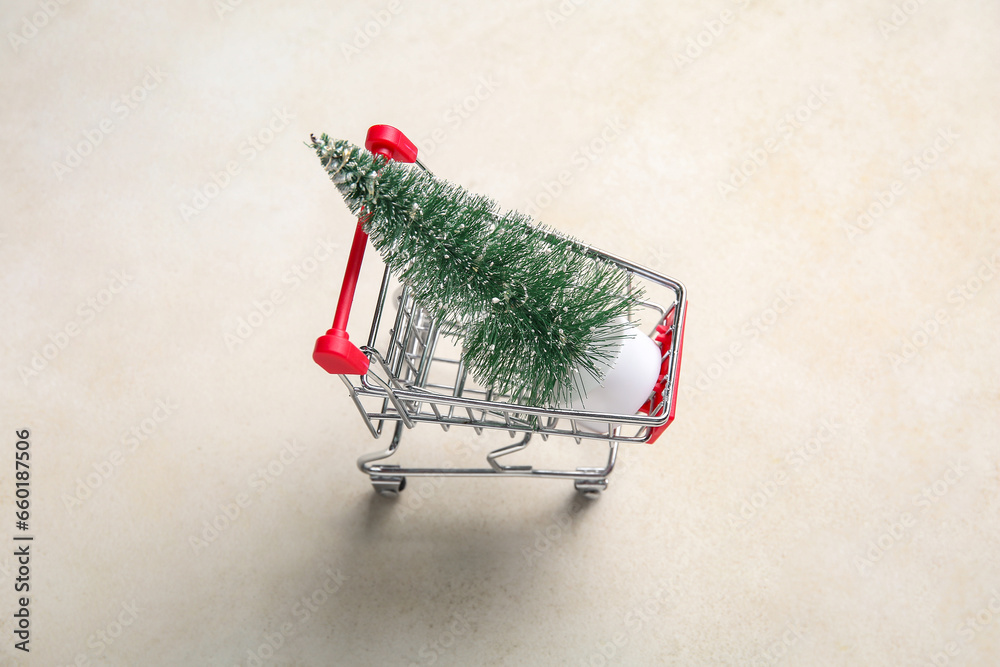 Shopping cart with Christmas tree on beige background