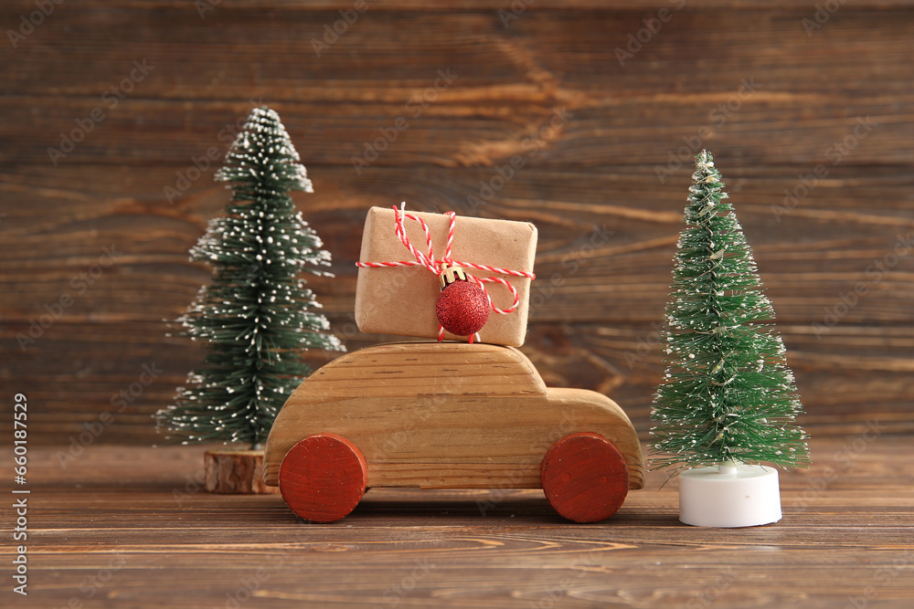 Christmas trees with toy car and gift box on wooden background