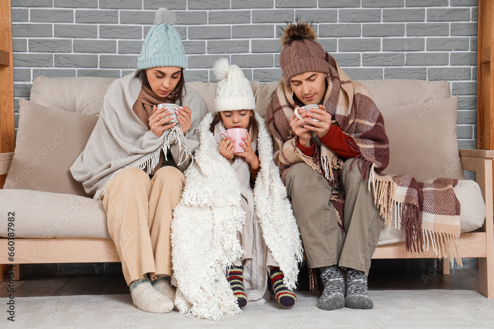 Frozen family in warm clothes drinking tea at home with lack of heating