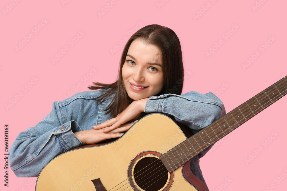 Pretty young woman with acoustic guitar sitting on pink background