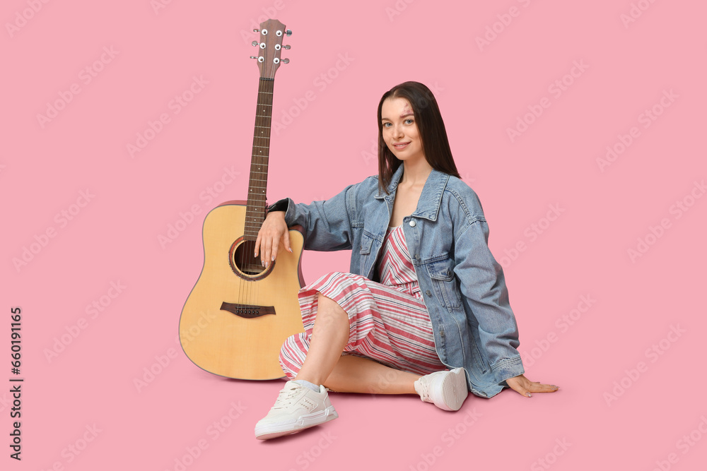 Pretty young woman with acoustic guitar sitting on pink background